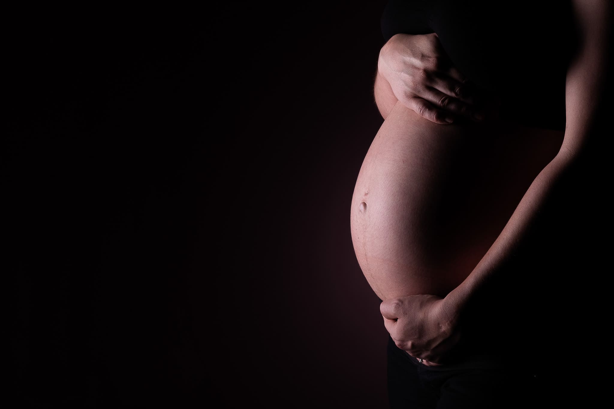 Photographe grossesse geneve - ventre de femme enceinte en gros plan avec les mains.