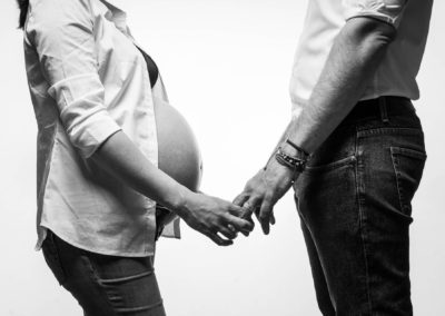Photographe grossesse geneve - couple qui se tient par les mains en noir et blanc sur fond blanc.
