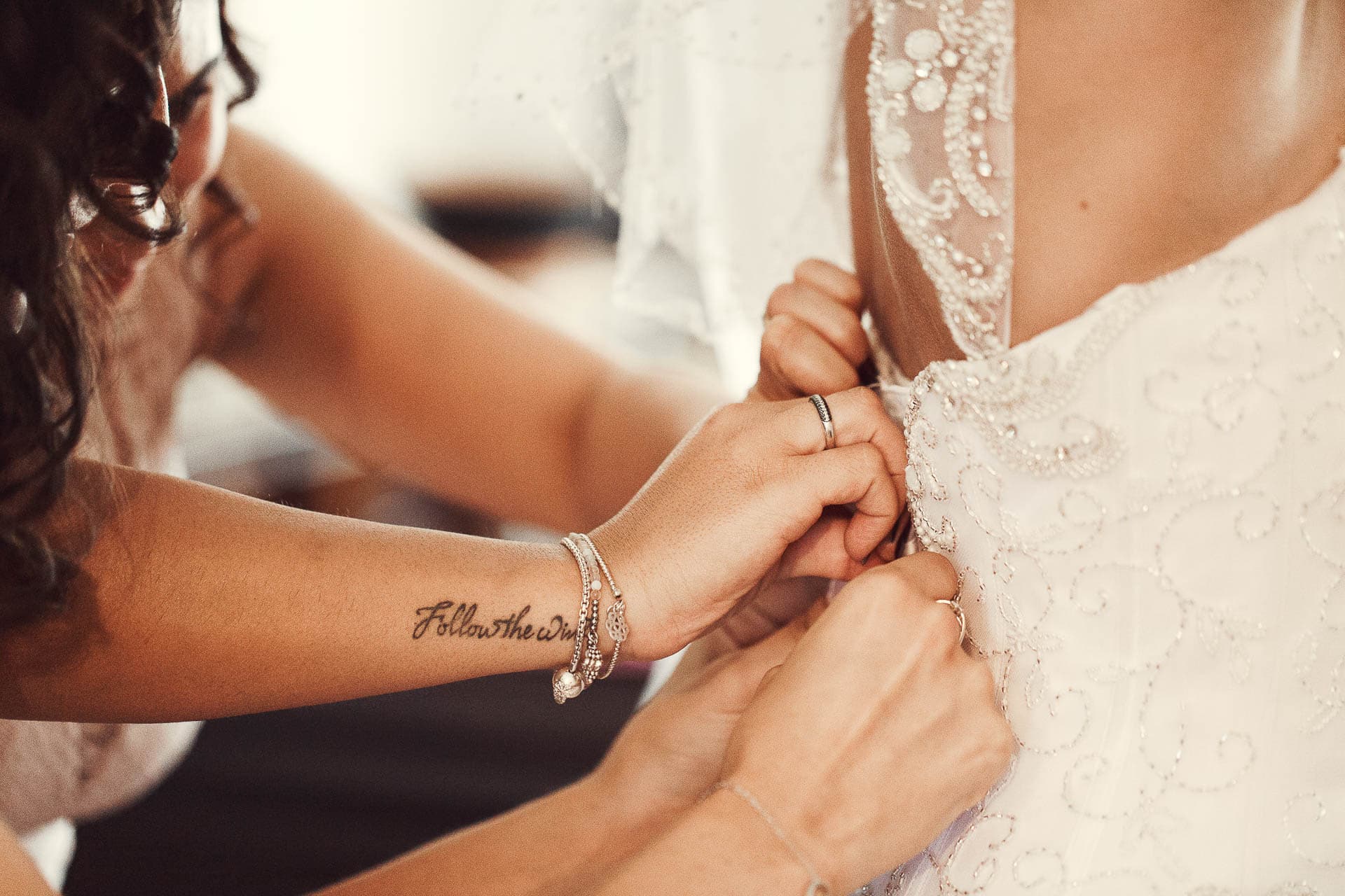 photographe mariage geneve - les demoiselles d'honneur qui ferment la robe de la mariée en gros plan sur les mains.